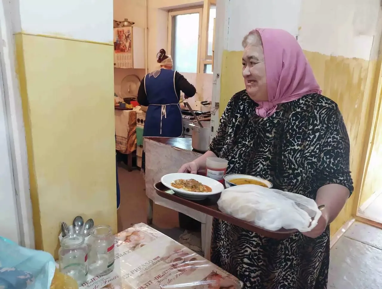 Eine Mitarbeiterin trägt ein Tablett mit Essen durch die Küche der Armenküche.
