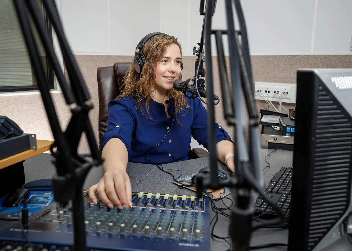 Eine Moderatorin sitzt mit Kopfhörern am Mischpult eines Radiostudios und spricht ins Mikrofon.
