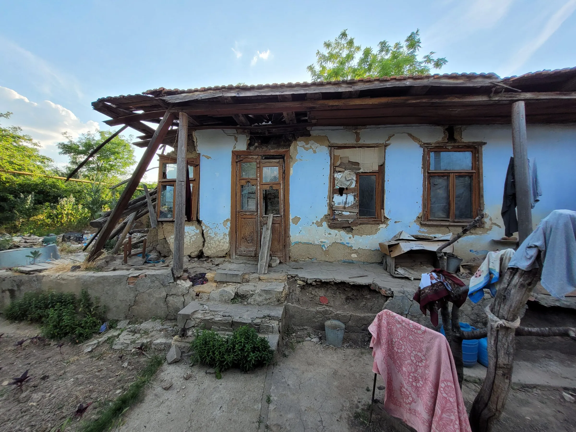 Ein baufälliges Haus mit abblätterndem Putz, notdürftig geflickten Fenstern und schiefem Vordach.