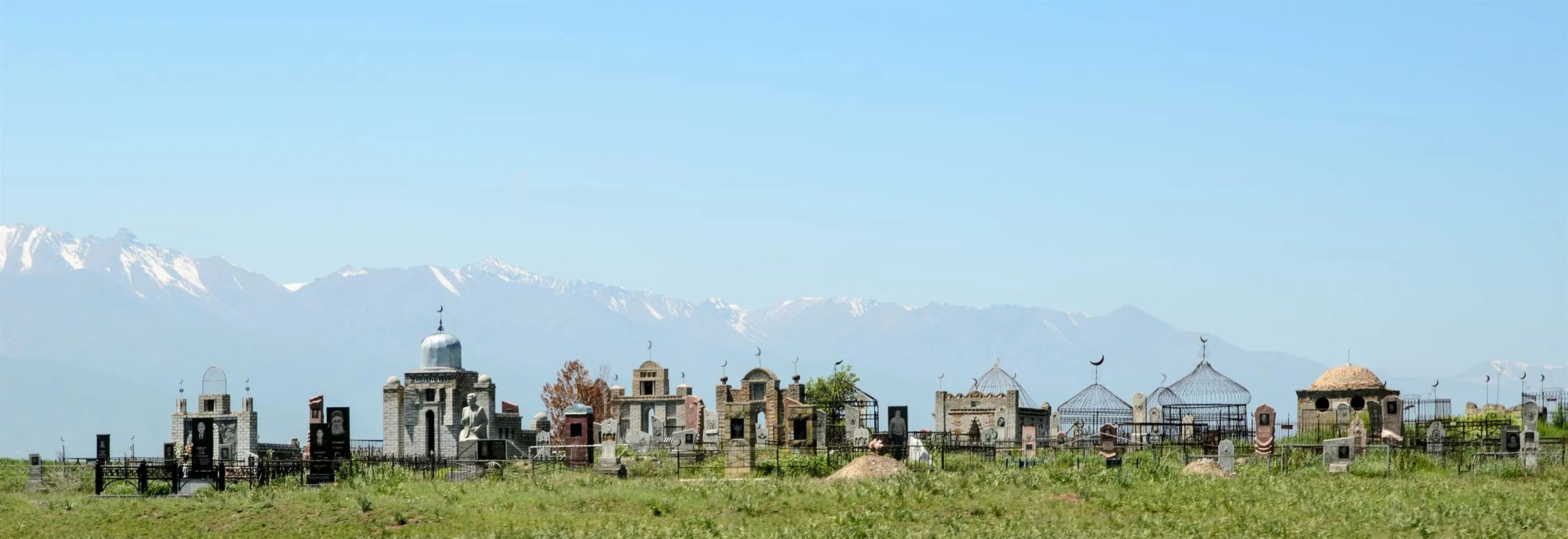 Ein Friedhof am Ortsrand vor einer weiten Bergkette, Grabmale mit Kreuzen und Halbmonden nebeneinander.