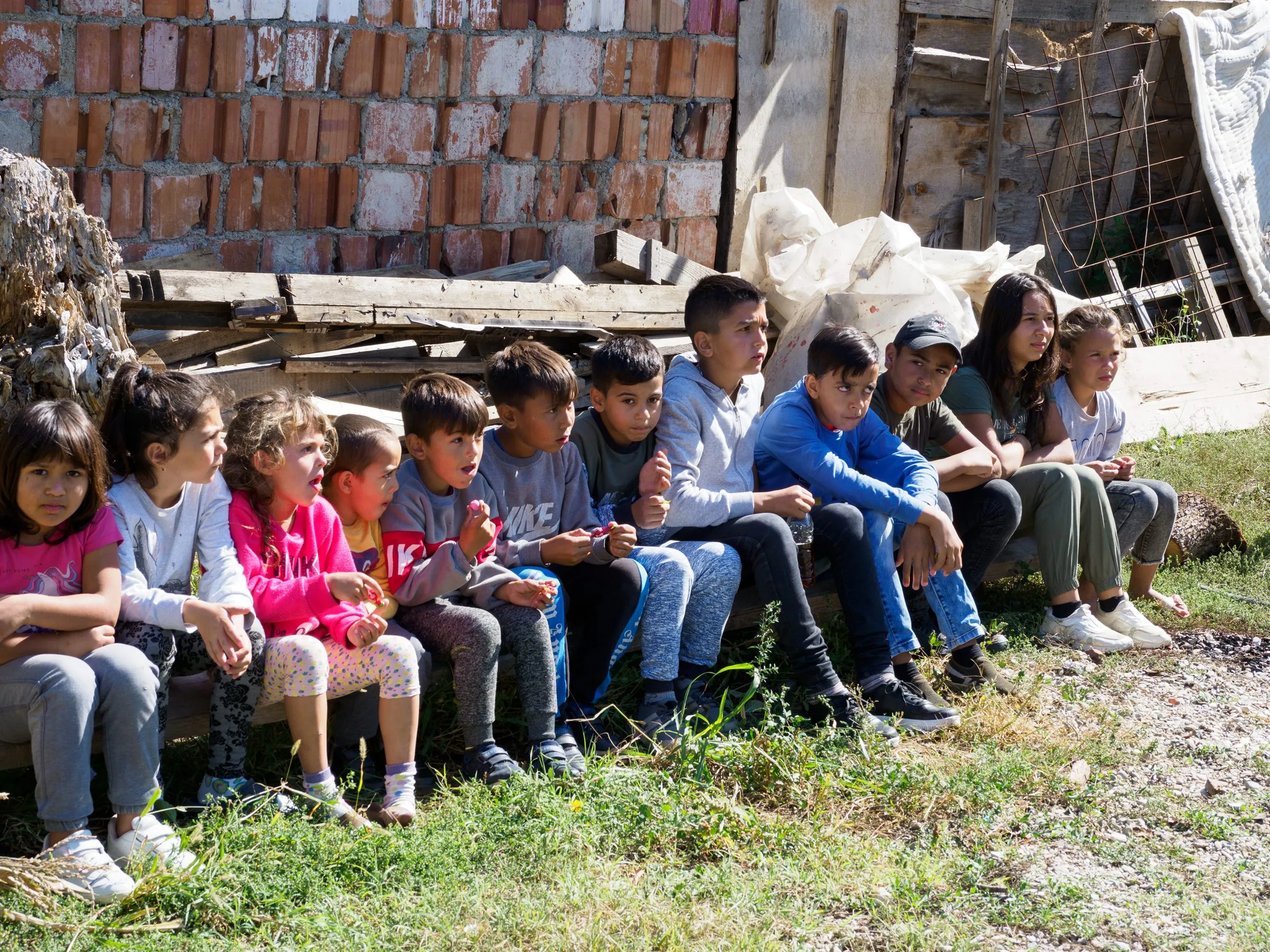 Bei einem Partnerbesuch im Kosovo: Kinder und Jugendliche sitzen draußen nebeneinander auf einer Bank und hören gespannt zu.
