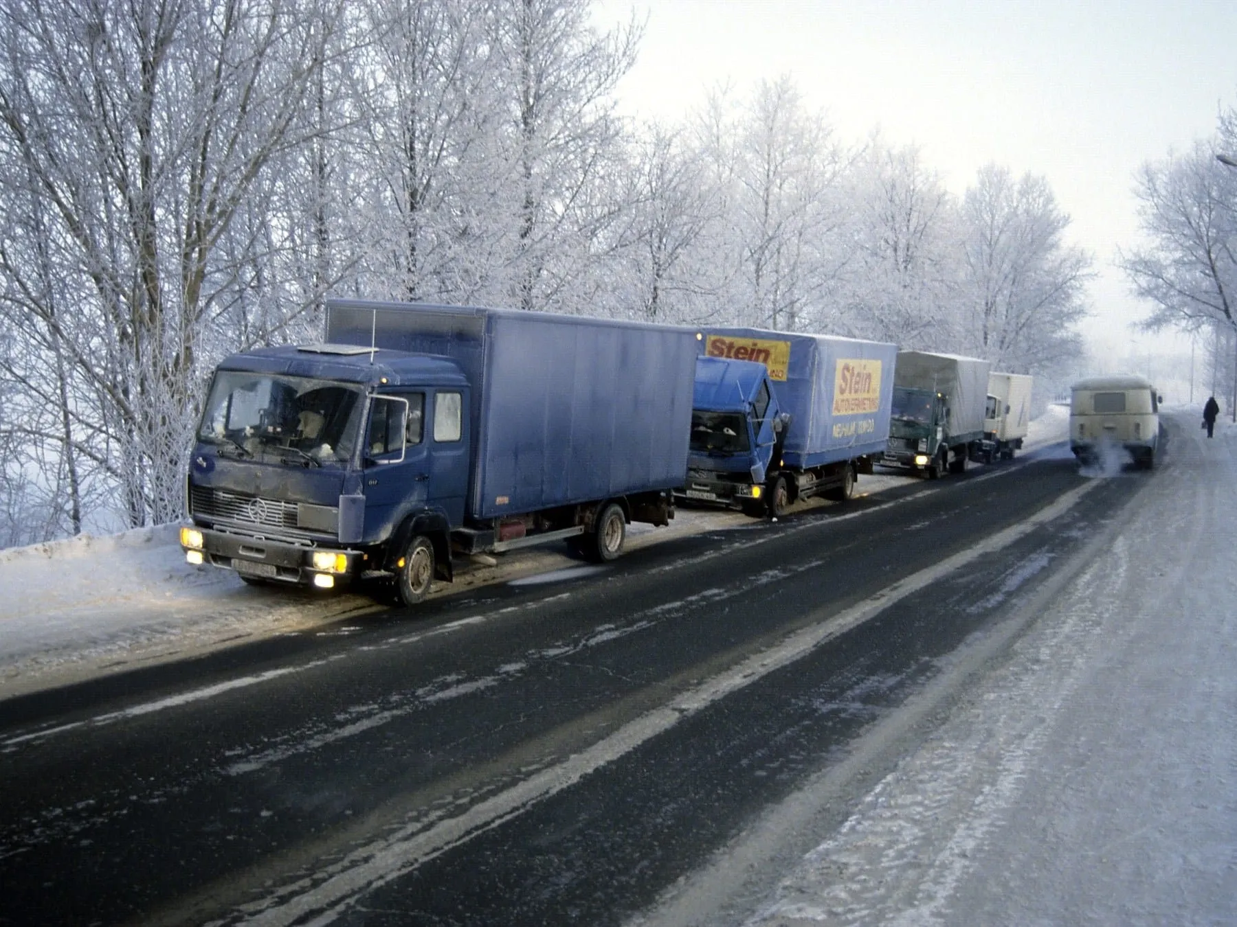 Vier Lastwagen eines Hilfstransports stehen 1994 bei Frost an einer verschneiten Landstraße.