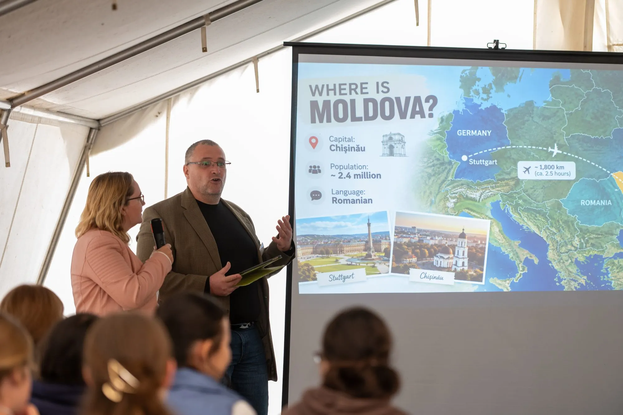 Bericht im Zelt: zwei Personen sprechen vor einer Leinwand mit der Frage „Where is Moldova?“ und einer Karte.