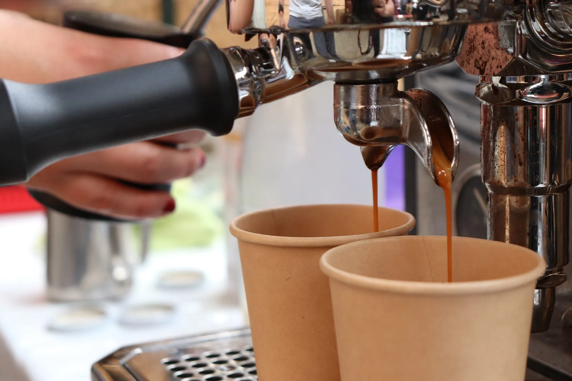 Aus der Siebträgermaschine läuft Kaffee in zwei Pappbecher.