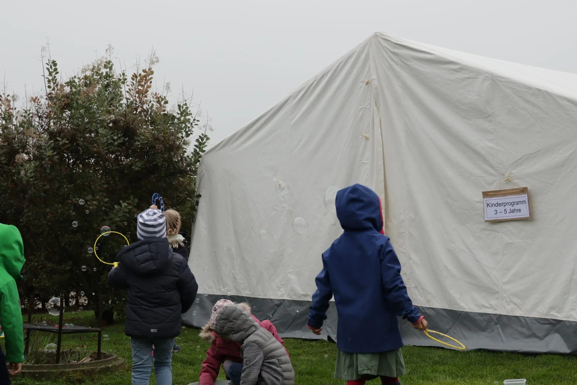 Kinder mit Seifenblasen vor dem Zelt des Kinderprogramms, am Eingang ein Schild mit der Altersgruppe.