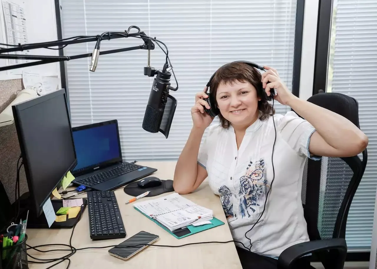Eine Sprecherin sitzt mit Kopfhörern vor dem Mikrofon im Studio.